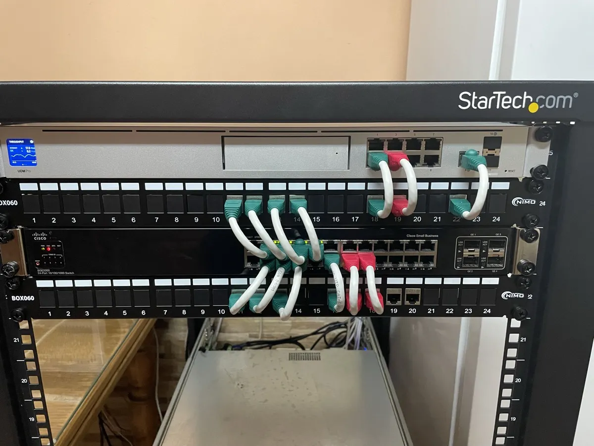 Armario de comunicaciones con router UniFi Dream Machine Pro, switch gestionado y dos paneles de parcheo de 24 puertos, con los latiguillos ordenados por color.